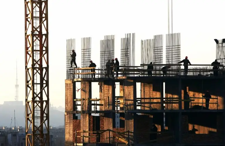 Construction workers on a building framework at sunset.